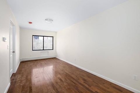a living room with white walls and wood floors and a window